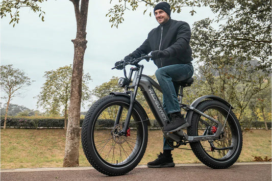 Overcast park lifestyle shot of a smiling male rider sitting on matte grey RZOGUWEX S7 integrated-frame fat tire e-bike along a tree-lined paved park path.