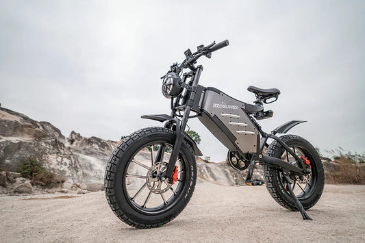Front three-quarter static shot of matte grey RZOGUWEX X5S retro fat tire electric dirt bike parked on rocky desert terrain under overcast sky.