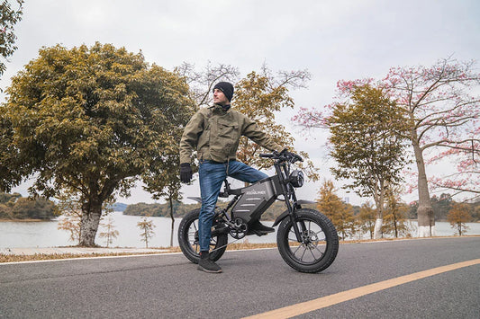 Lakeside roadside lifestyle shot of a man posing beside matte grey retro RZOGUWEX X5S fat tire electric cruiser bike, lined with autumn foliage trees and calm lake waters.