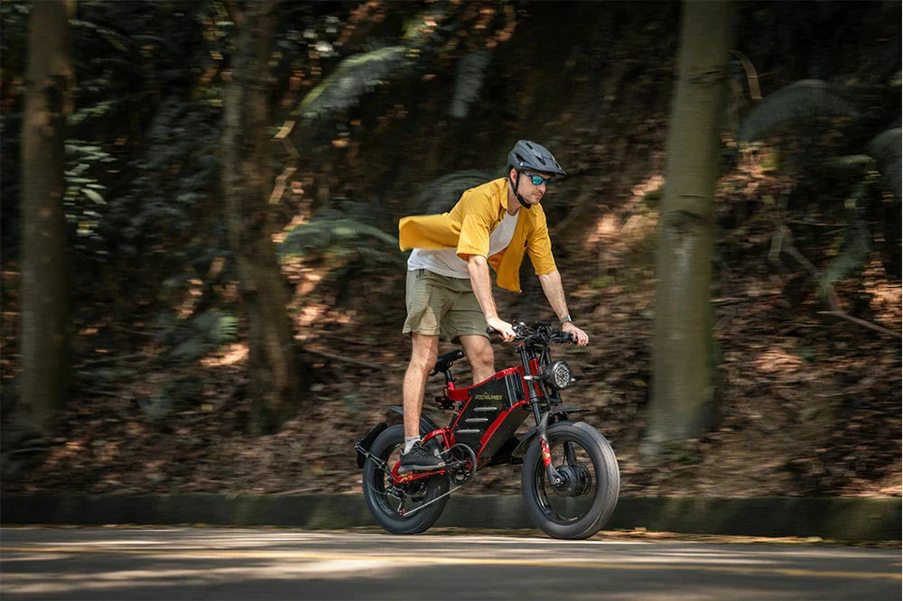 A man with a helmet rides a bold red‑black e‑bike swiftly along a sun‑dappled forest road.