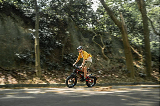 RZOGUWEX X7 red-black foldable fat tire e-bike ridden by a man speeding through a shaded forest mountain road.