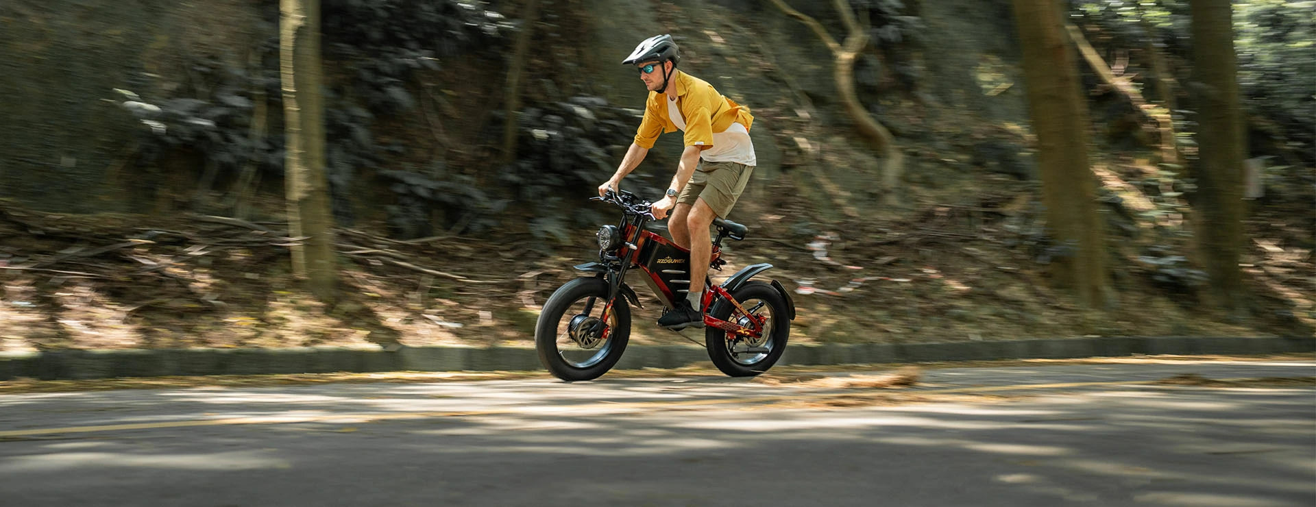 Motion-blur forest trail shot of a man riding red-black RZOGUWEX X7 retro fat tire electric bike along shaded woodland asphalt road.